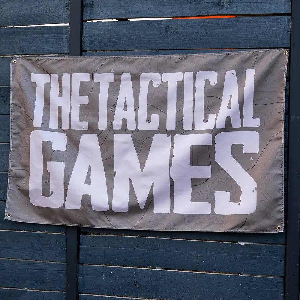 A rectangular gray horizontal banner with the words 'THE TACTICAL GAMES' in large white block letters,